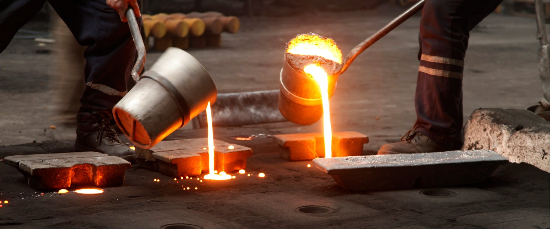 Molten metal being poured into ingots in a foundry by workers in protective gear.
